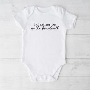 May include: White baby onesie with black text that reads "I'd rather be on the boardwalk".