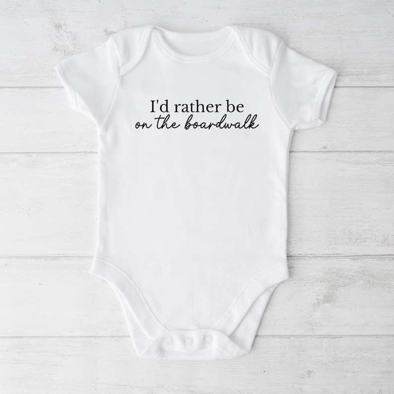 May include: White baby onesie with black text that reads "I'd rather be on the boardwalk".