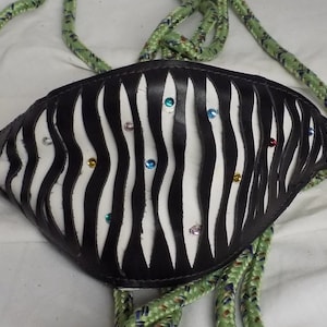 Puede incluir: Un cabezada de cuero negro y blanco con estampado de cebra con brillantes de colores. La cabezada está unida a una cuerda verde.