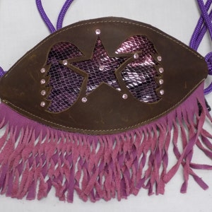 Puede incluir: Un cabezal de cuero marrón con un diseño de estrella rosa y morada y flecos. El cabezal tiene una cuerda morada atada a él.