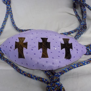 Puede incluir: Un cabestro de cuero morado con tres recortes de cruz marrones y diamantes de imitación. El cabestro está hecho de cuerda trenzada.