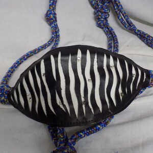 Puede incluir: Un cabestro de cuero negro y blanco con estampado de cebra con diamantes de imitación. El cabestro está unido a una cuerda azul y blanca.