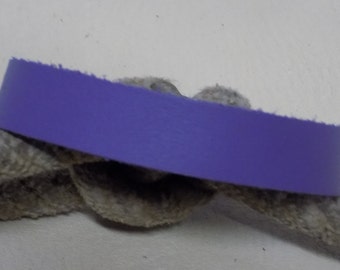 May include: A close-up of a purple leather strap with a frayed edge. The strap is lying on a grey, textured surface.