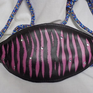 Puede incluir: Un bolso de cuero negro con estampado de cebra rosa y pedrería. El bolso tiene un asa de cuerda.