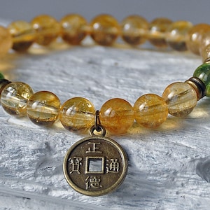 May include: A gold and green beaded bracelet with a gold Chinese coin charm. The coin has the Chinese characters "Zheng" (正) and "Dao" (道) on it.