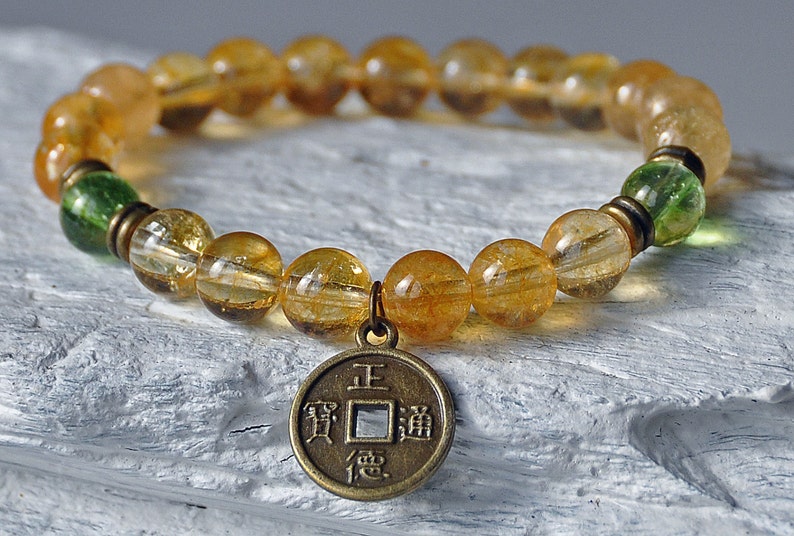 May include: A gold and green beaded bracelet with a gold Chinese coin charm. The coin has the Chinese characters "Zheng" (正) and "Dao" (道) on it.