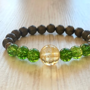 May include: A bracelet made of dark gray, brown, and green beads. The bracelet has a large, round, clear bead with gold flecks in the center.