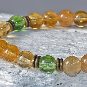 May include: A gold and green beaded bracelet with a gold coin charm. The bracelet is made with citrine and green aventurine beads.