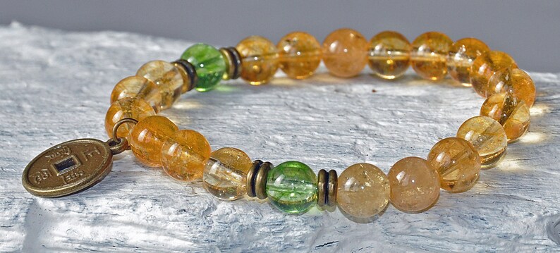 May include: A gold and green beaded bracelet with a gold coin charm. The bracelet is made with citrine and green aventurine beads.