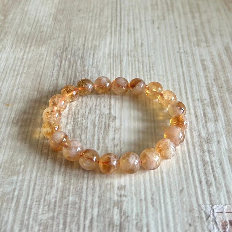 May include: A bracelet made of round, orange-colored beads with a light brown background.