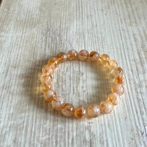 May include: A bracelet made of round, orange and white beads. The beads have a translucent, cloudy appearance.