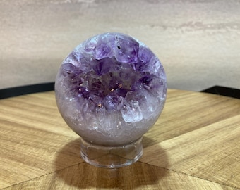 May include: A purple amethyst geode sphere on a clear stand. The geode is filled with crystals and has a natural, rough exterior.