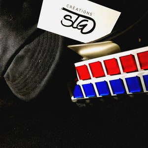 Peut inclure: Une console de commande argentée et blanche avec des boutons rouges et bleus. La console est sur une surface noire avec un chapeau noir et une carte blanche avec le texte "CREATIONS STG".