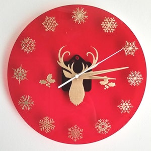 May include: A red wall clock with gold snowflake accents and a gold reindeer head in the center. The clock hands are gold and white. The clock is a festive holiday decoration.