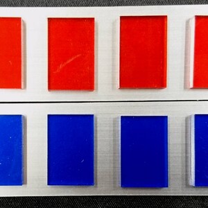 May include: A silver metal badge with six rectangular colored panels. The top row has four red panels and the bottom row has four blue panels.
