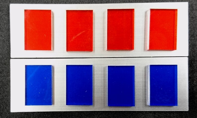May include: A silver metal badge with six rectangular colored panels. The top row has four red panels and the bottom row has four blue panels.