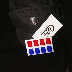 May include: A black cap with a silver pin and a white card with the text "SIG CREATIONS". A silver metal patch with six red and blue squares.