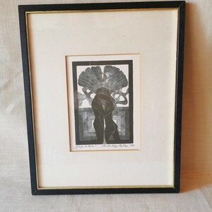 May include: A framed black and white print featuring two figures embracing under a large ginkgo leaf. The artwork is titled "Gingo Biloba" and signed by Anita Hepp Pallas 1990. The piece is housed in a black frame with a cream-colored mat.