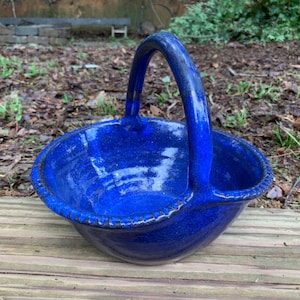 May include: A blue ceramic basket with a handle. The basket has a scalloped edge and a speckled glaze.