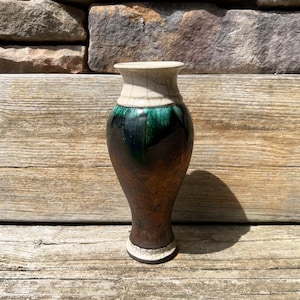 May include: A small, dark brown ceramic vase with a green and white glaze. The vase has a rounded body and a narrow neck.