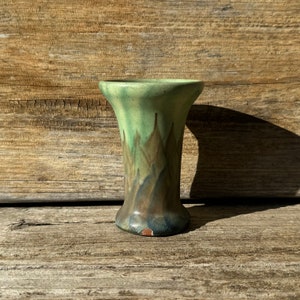 May include: A small, green and brown ceramic vase with a flared top and a unique glaze pattern.