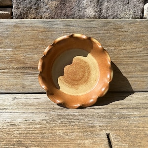 May include: A small, brown ceramic pie plate with a scalloped edge. The plate has a light brown glaze with a speckled pattern.