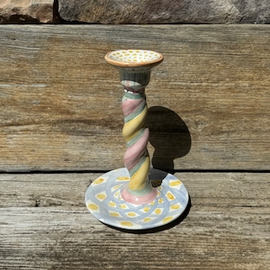 May include: A ceramic candlestick with a twisted, multi-colored design. The base is a circular plate with a swirling pattern in shades of blue, yellow, and white.