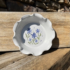 May include: A white ceramic pie plate with a scalloped edge and a blue and green floral design. The flowers are stylized and have five petals.