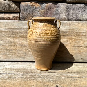 May include: A brown ceramic vase with two handles. The vase has a textured surface and a light brown glaze.