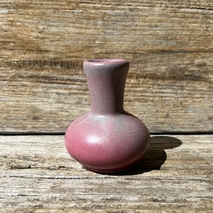 May include: A small, pink and gray ceramic vase with a rounded body and a narrow neck.