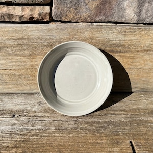 May include: A white ceramic plate with a slightly rippled edge. The plate is sitting on a wooden surface.