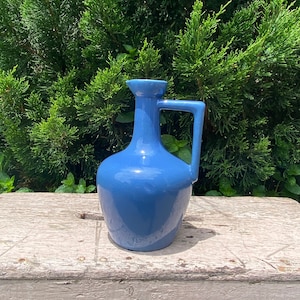 May include: A blue ceramic pitcher with a handle. The pitcher has a rounded body and a narrow neck.