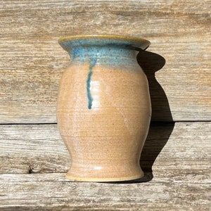 May include: A light brown ceramic vase with a blue glaze on the top rim and a blue streak down the side.