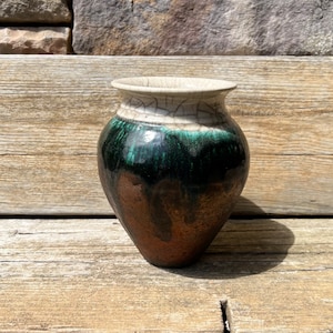 May include: A small, green and brown ceramic vase with a white crackle glaze. The vase has a rounded body and a wide opening.