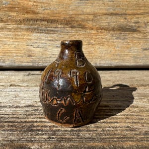 May include: A small, brown, ceramic jug with the inscription "1946 Santa CA" carved into the side.