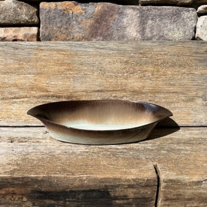 May include: A brown and white glazed ceramic serving dish with a rounded oval shape. The dish has a slight lip on each end.