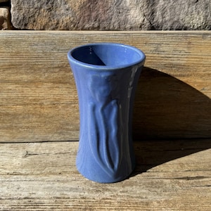 May include: A blue ceramic vase with a textured design. The vase is tall and narrow, with a rounded base and a flared top.
