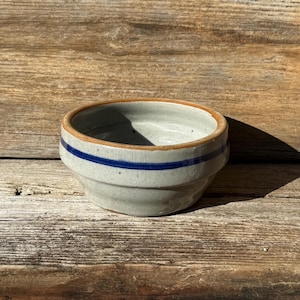 May include: A small, gray ceramic bowl with a brown rim and two blue stripes around the top.