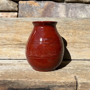 May include: A small, red, ceramic vase with a rounded body and a textured, ribbed design. The vase has a glossy finish.