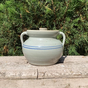 May include: A gray ceramic crock with a lid and two handles. The crock has a blue stripe around the middle.