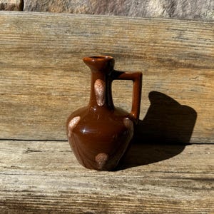 May include: A small brown ceramic pitcher with a white speckled design. The pitcher has a rounded body and a handle.