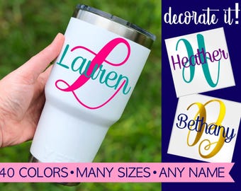 May include: A white stainless steel tumbler featuring a custom pink and teal script name decal. The image includes text that reads decorate it!, 40 COLORS • MANY SIZES • ANY NAME, and examples of names Heather and Bethany in script.