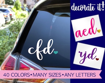 May include: A white vinyl decal with the lowercase letters cfd and a small teal heart applied to a car window. Additional examples show the letters aed in pink with a gold heart and rjd in purple with a red heart. Text reads decorate it!