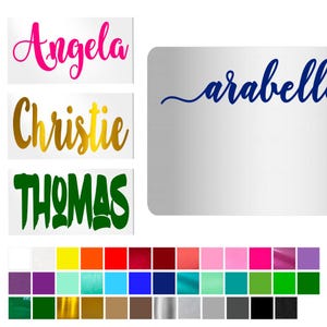 May include: A collection of personalized name decals in various colors. The names "Angela" in pink, "Christie" in gold, and "Thomas" in green are displayed on white rectangles. A blue "arabella" decal is also shown. A color palette of vinyl options is at the bottom.