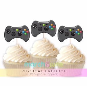 May include: Twelve black and green video game controller cupcake toppers. The toppers are on top of cupcakes with white frosting.