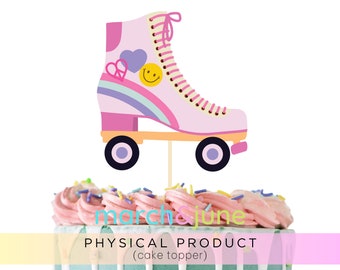 May include: A pink roller skate cake topper with a rainbow, heart, and smiley face design. The cake topper is on a wooden stick and is placed on top of a cake with pink frosting and sprinkles. The text "march & june" and "PHYSICAL PRODUCT (cake topper)" are visible.