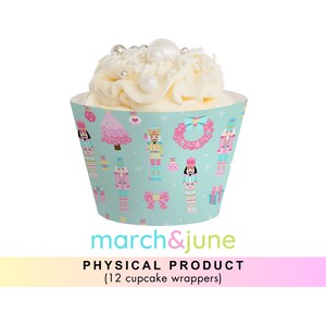Könnte beinhalten: Ein Set mit 12 Cupcake-Verpackungen mit einem fantasievollen Nussknacker-Motiv. Die Verpackungen sind türkisblau mit rosa, weißen und goldenen Akzenten. Das Design umfasst Nussknacker-Soldaten, Weihnachtsbäume, Kränze und Schleifen.
