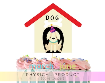 May include: A yellow dog wearing a party hat sits inside a red and white dog house cake topper. The dog house has the word "DOG" written on it.