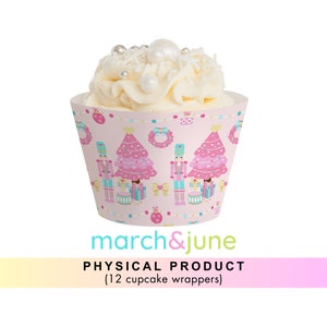 Könnte beinhalten: Rosa Cupcake-Verpackungen mit einem Nussknacker- und Weihnachtsbaum-Design. Die Verpackungen haben einen rosa Hintergrund mit goldenen, blauen und weißen Akzenten. Der Text "march&june" ist auf der Unterseite der Verpackungen aufgedruckt. Der Text "PHYSICAL PRODUCT (12 cupcake wrappers)" ist unter dem Markennamen aufgedruckt.