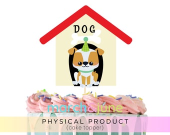 May include: A cake topper featuring a cartoon dog inside a dog house with the word "DOG" above. The topper is on a cake with pink frosting and sprinkles. The text "march & june" and "PHYSICAL PRODUCT (cake topper)" are also visible.